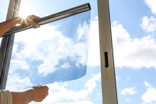 Two hands of a man opening a tint film in front of a window for making a residential window tinting service